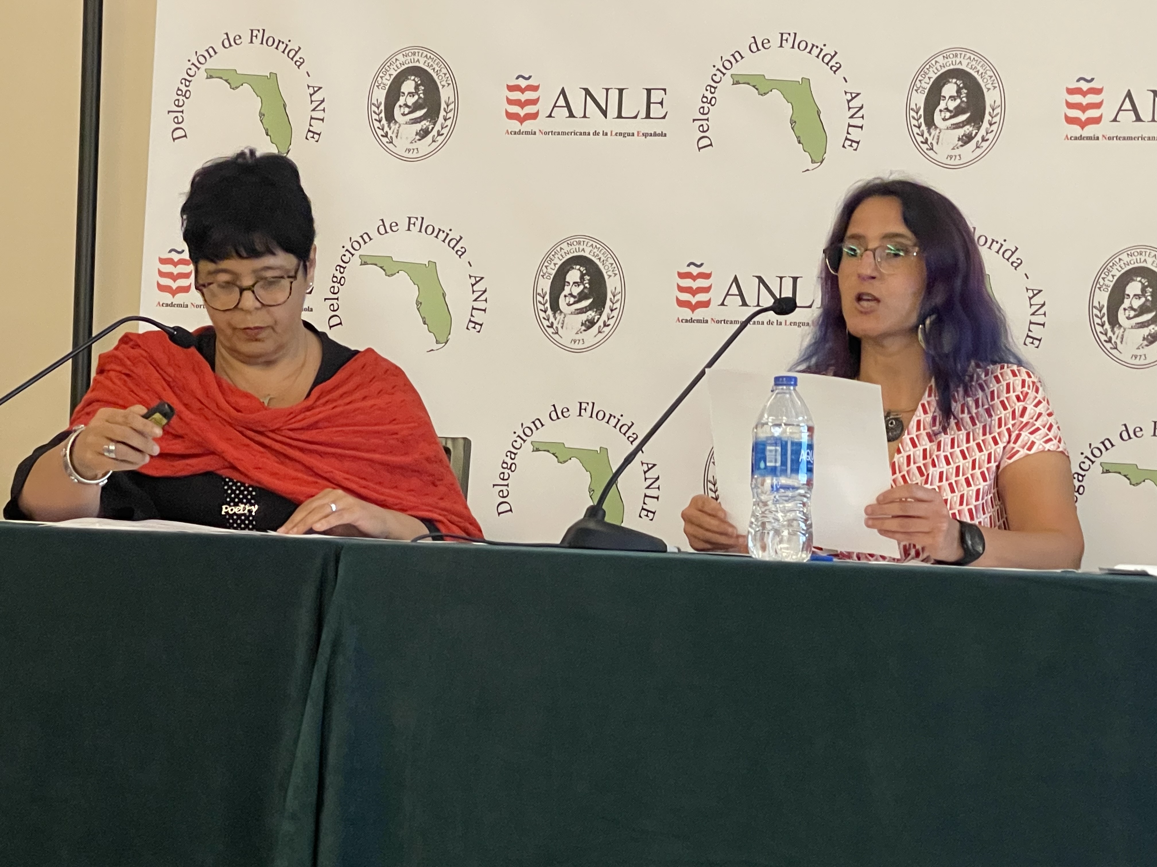 The image shows Aurora Humarán and Erika Cosenza seated at a table with microphones. Behind them, ANLE's logo. Erika is speaking.